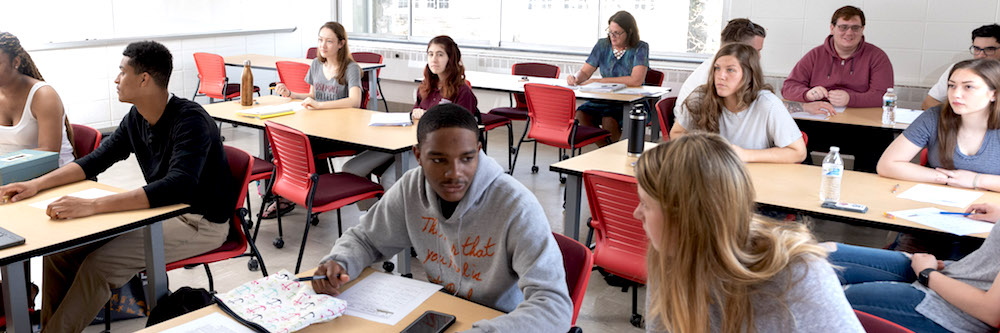 A classroom of undergraduate students of various ethnic backgrounds an gender presentations.