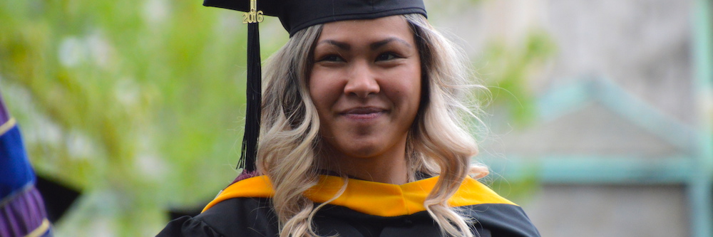 Adult student wears a cap and gown. She is of asian descent and has tan skin and bleached hair.