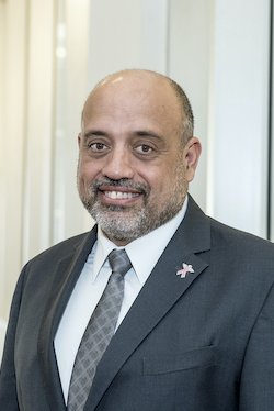 Dr. Randolph Merced, middle-aged man with light brown skin in a suit and tie. He is bald and has a beard.