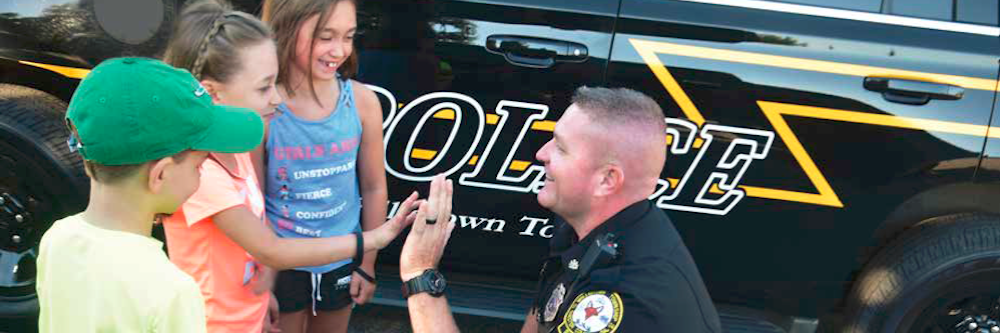 a police officer gives three young girls a high-five in front of his squad car. They are all caucasion.