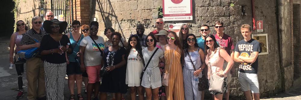 Global Studies program, in which a group of adult students of various age and ethnic background stand in front of a old grey brick wall in Italy.