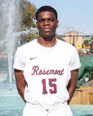 Tobi Joshuasville, an African-American male with short black hair, stands outside wearing a Rosemont College basketball jersey.