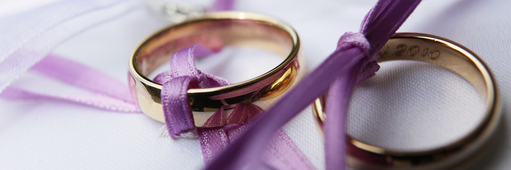 Image of gold wedding rings tied together with purple ribbon.